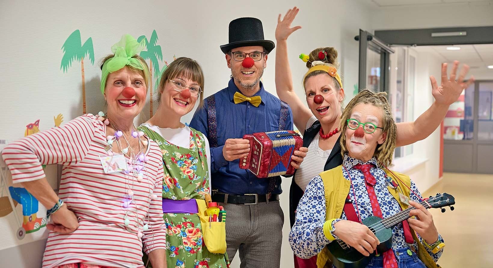 Eine Gruppe von Klinikclowns steht auf dem Flur der Kinderklinik am Städtischen und lacht in die Kamera.