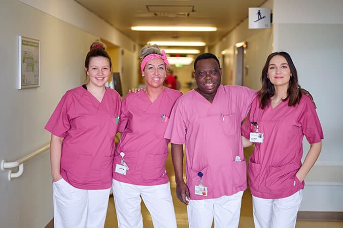 Vier Pflegekräfte stehen als Team im Stationsflur des Krankenhauses und lächeln in die Kamera.