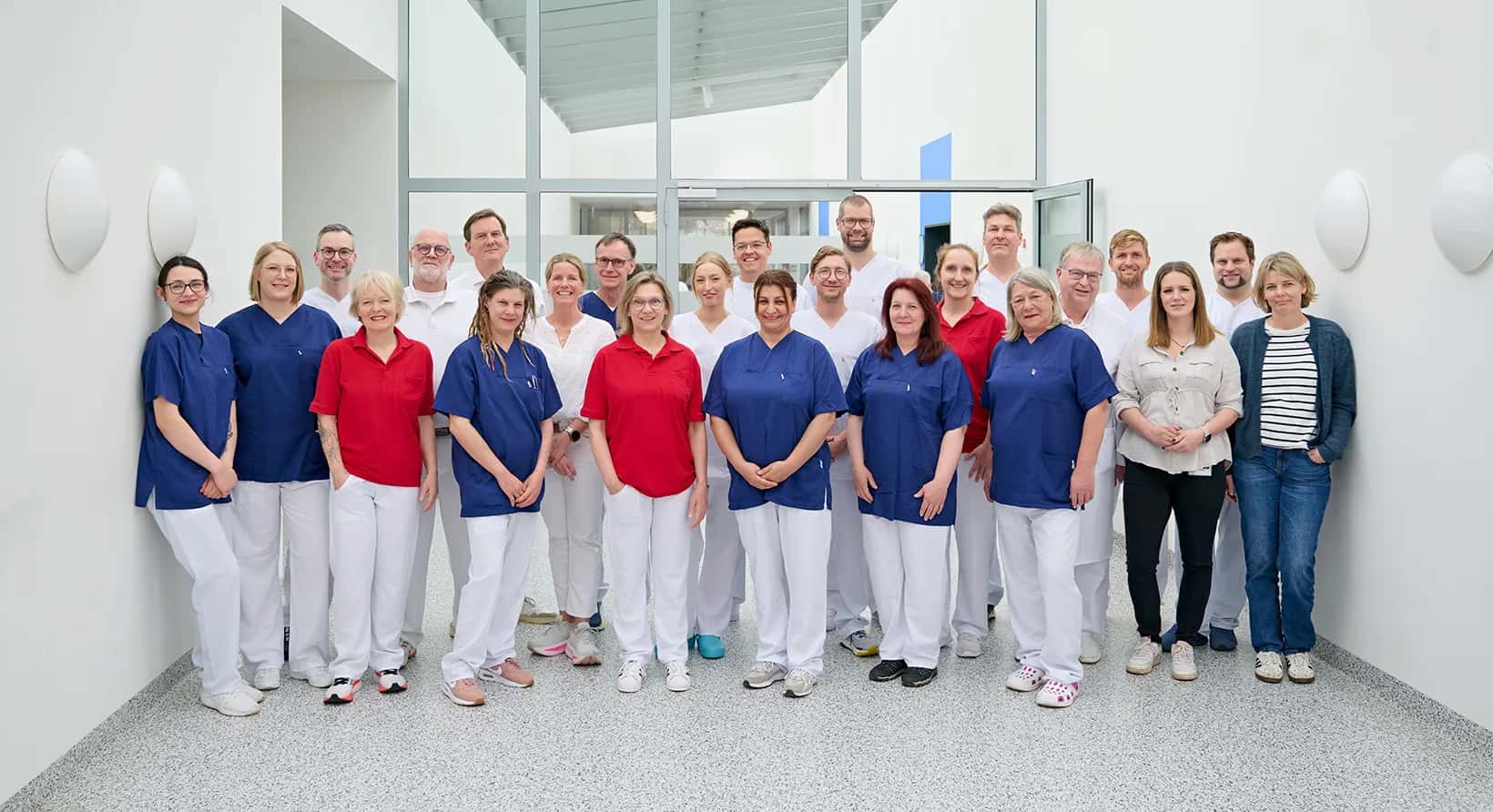 Ärzte, Pflegekräfte und weiteres Personal der Klinik für Orthopädie und Unfallchirurgie, am Städtischen Krankenhaus in Kiel, stehen in einer Gruppe zusammen und lächeln in die Kamera.