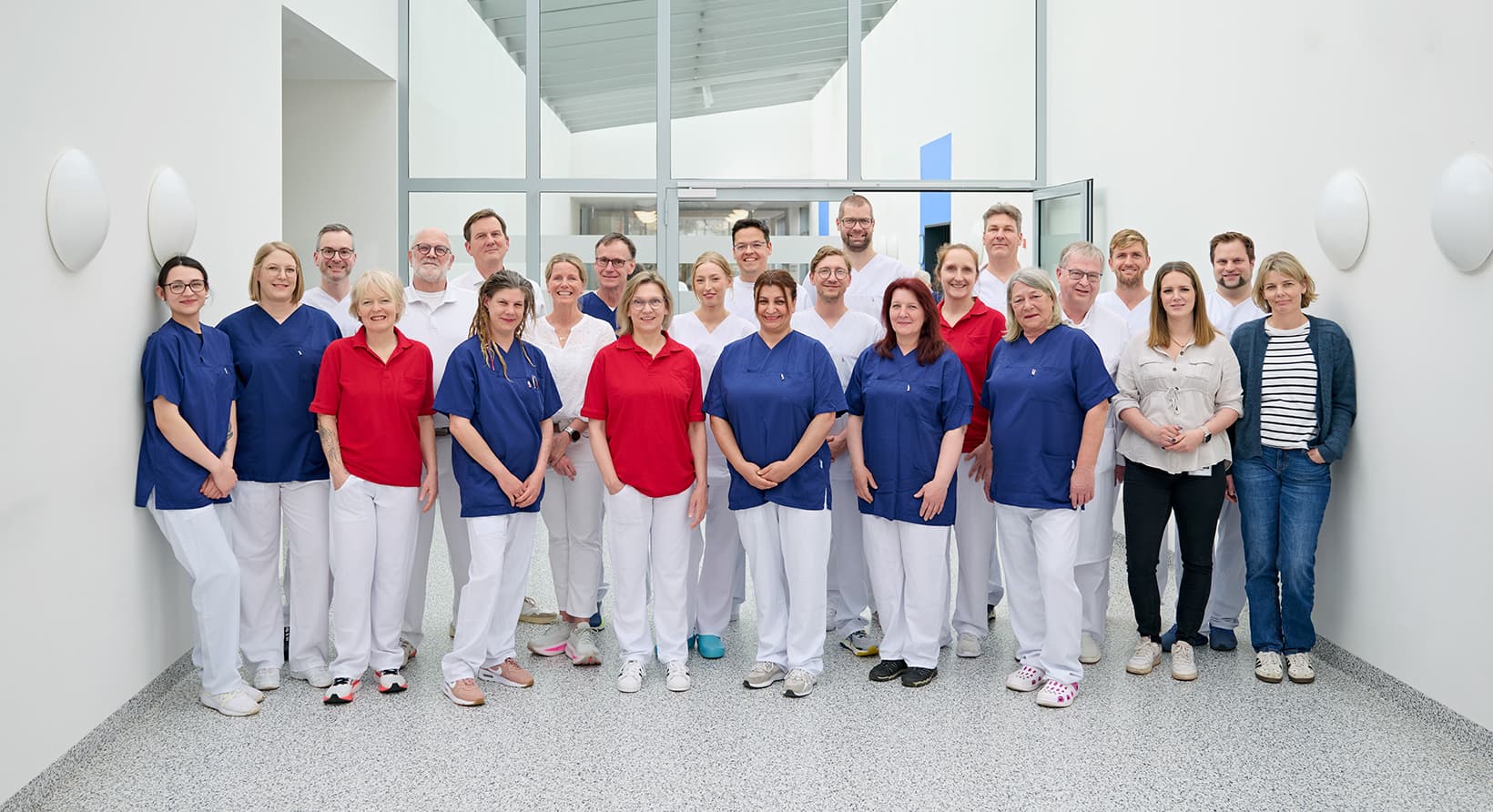 Ärzte, Pflegekräfte und weiteres Personal der Klinik für Orthopädie und Unfallchirurgie, am Städtischen Krankenhaus in Kiel, stehen in einer Gruppe zusammen und lächeln in die Kamera.