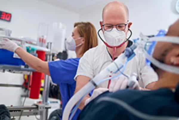 Ein Arzt in der zentralen Notaufnahme versorgt einen Patienten und wird von einer Kollegin im Hintergrund unterstützt.