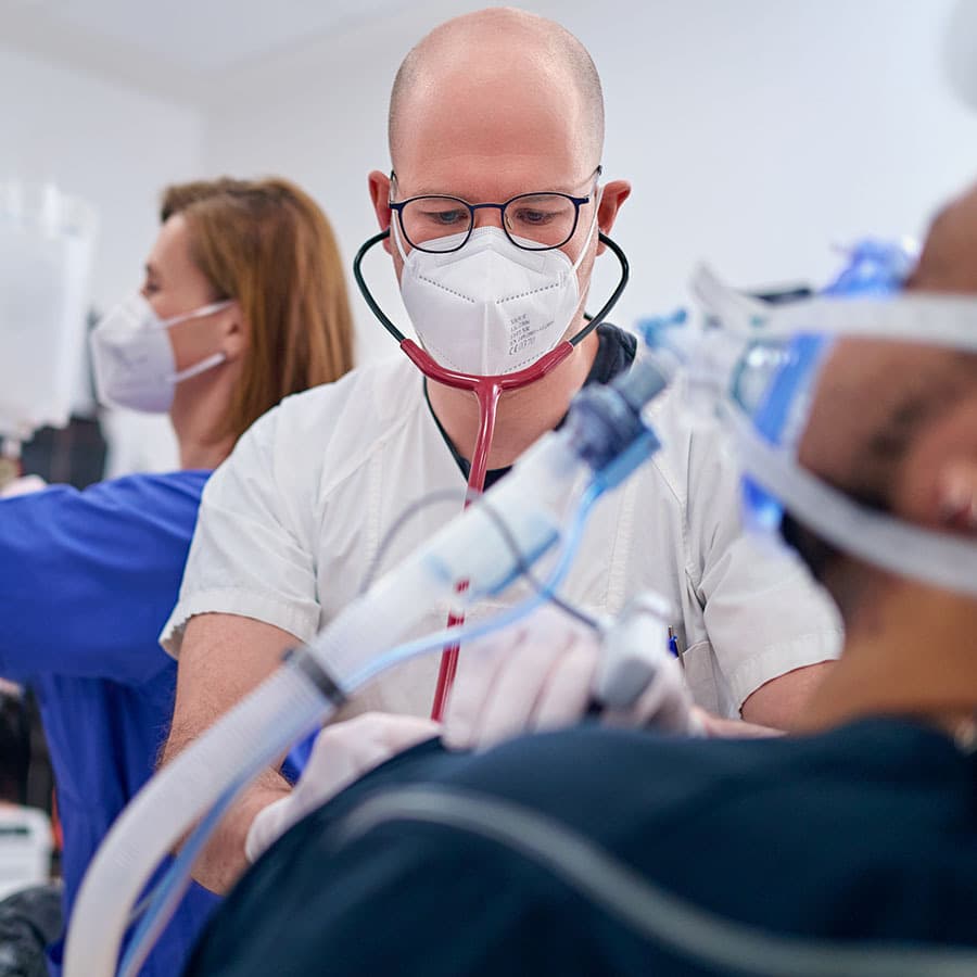 Ein Arzt in der zentralen Notaufnahme behandelt mit einer Kollegin einen Patienten. Der Patient wird mit einer Sauerstoffmaske mit Atemluft versorgt.