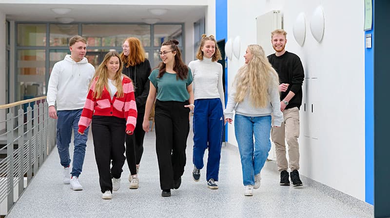 Auszubildene laufen in einer Gruppe einen Flur im SKK Bildungszentrum entlang und unterhalten sich untereinander.