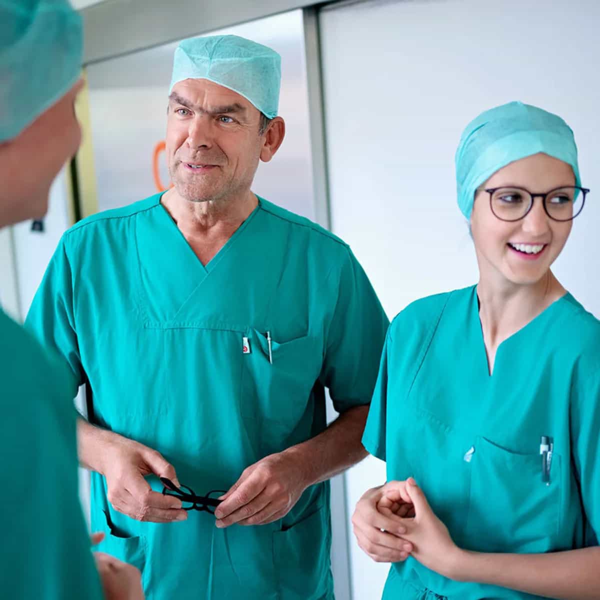 Zwei Auszubildende zu anästhesietechnischen Assistentinnen (ATA) stehen gemeinsam mit dem Chefarzt der Klinik für Anästhesie und Operative Intensivmedizin auf einem Flur und unterhalten sich.