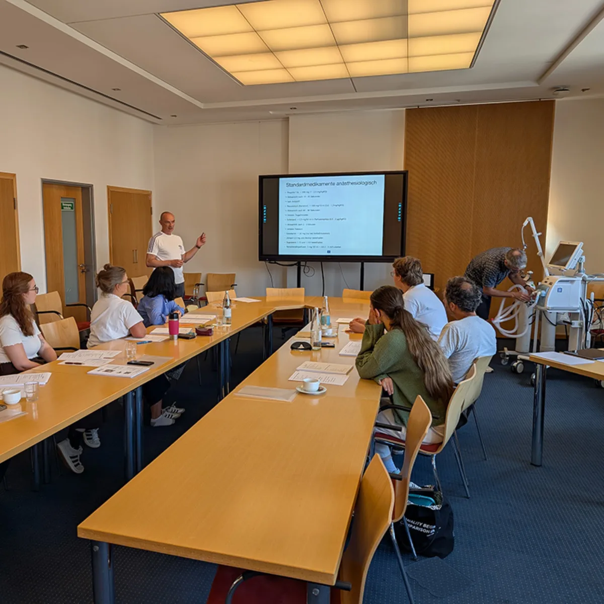 In einem Schulungsraum sitzen Mitarbeiter und Mitarbeiterinnnen aus dem Bereich Pflege Intensivmedizin zusammen und folgen einer Präsentation zum Thema Beatmung.