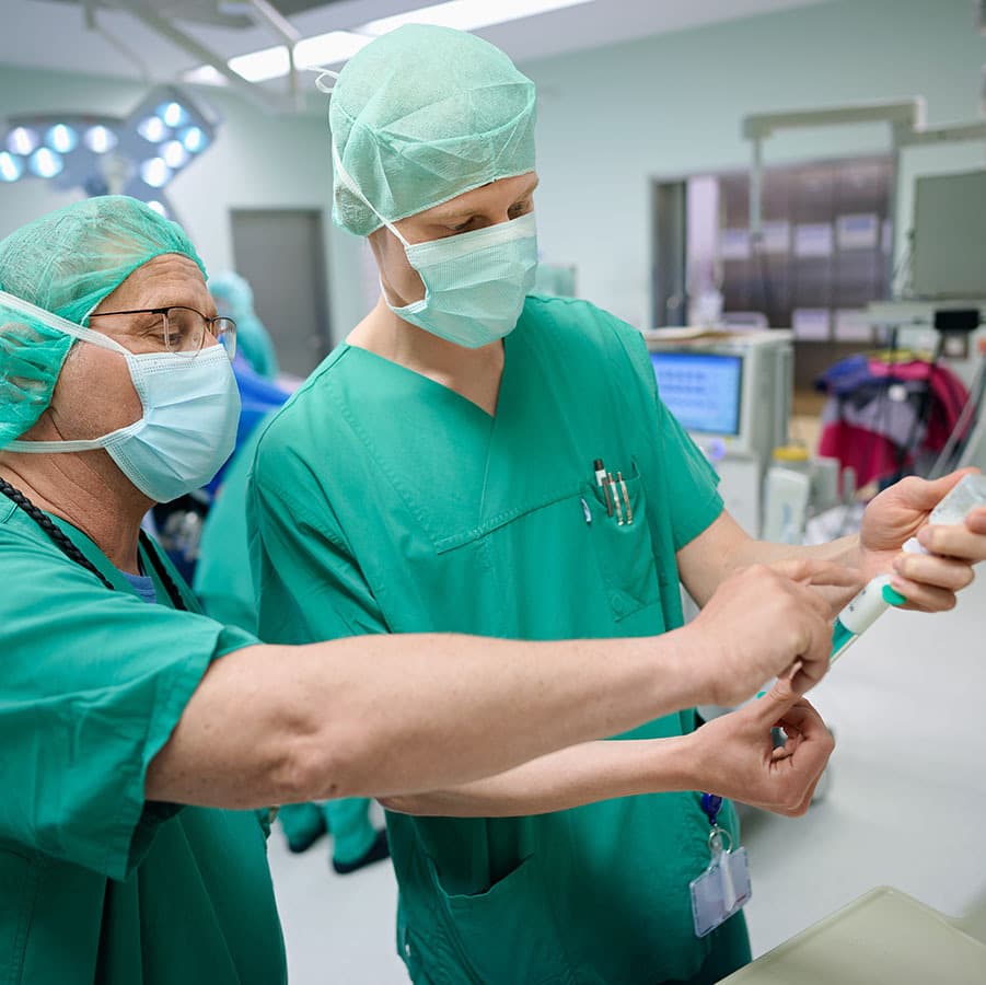 Zwei Anästhesietechnische Assistenten stehen im OP und bereiten eine Narkosespritze vor.